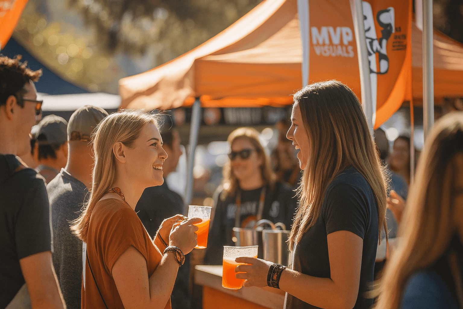 Attendees chatting at an outdoor event under an orange canopy featuring the MVP Visuals logo