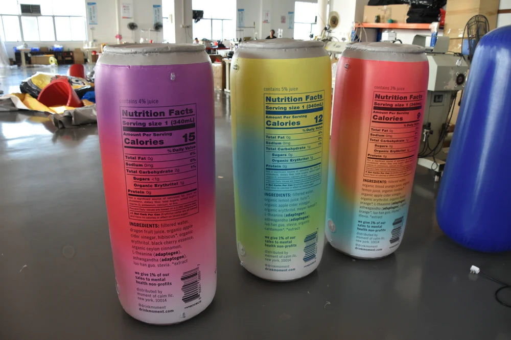 A set of three colorful inflatable cans with detailed nutritional information labels in a workshop setting