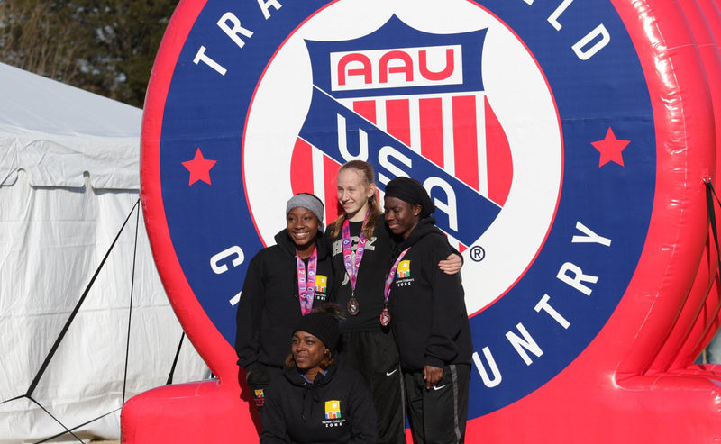 winners of AAU USA track and field cross country championship standing infront of inflatable logo