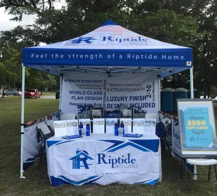 A trade show canopy with Riptide Builders branding, set in a park, showcasing home building services and promotions