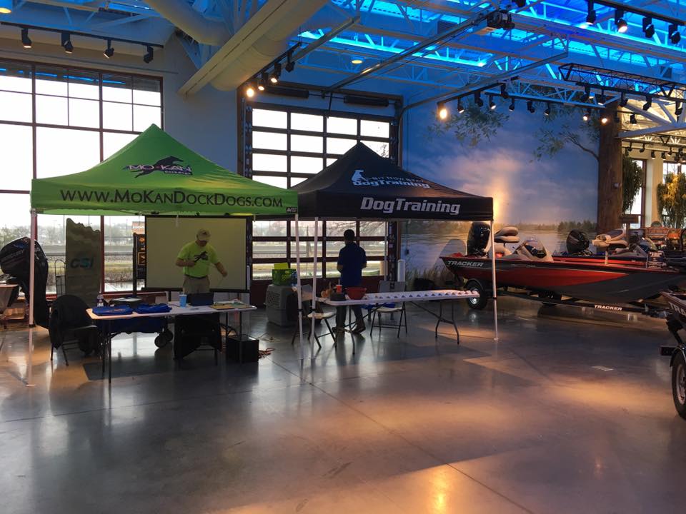 A vibrant green trade show tent with logo for MoKanDockDogs, set up for a dog training showcase indoors