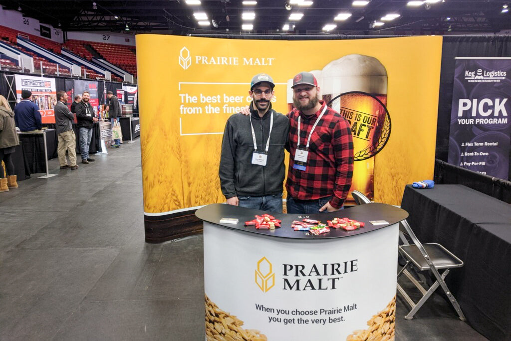 Prairie Malt event setup with informative display walls and podium, staff engaging with attendees