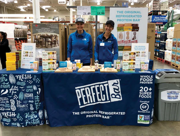 Custom trade show table cover with logo for Perfect Bar, displayed in a busy retail setting with representatives