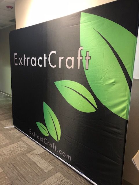 Fabric tension pop-up display featuring ExtractCraft branding with green leaf design on a trade show floor