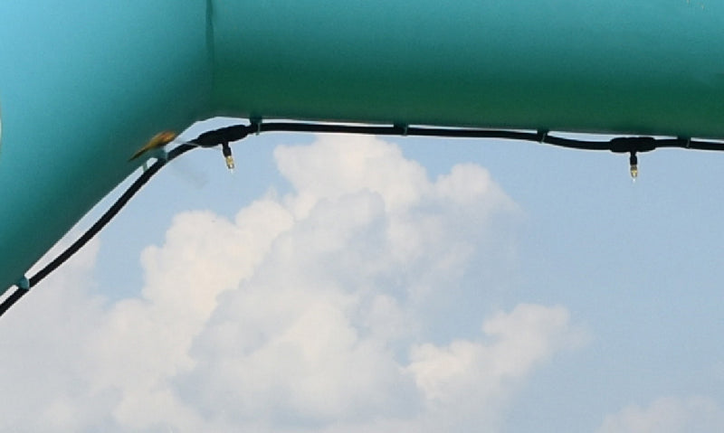 Close-up view of misting nozzles on a green inflatable arch against a cloudy sky, providing cooling at an outdoor event