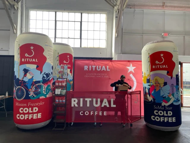 Giant inflatable protein-infused drink advertisement at a sunny farmers' market event