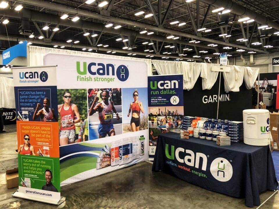 UCAN brand trade show booth with vibrant banner displays, promotional table, and product samples setup