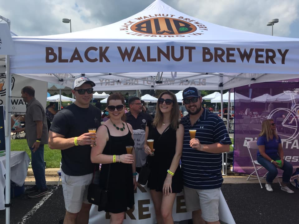 Group of friends enjoying drinks under 'Black Walnut Brewery' pop-up food tent