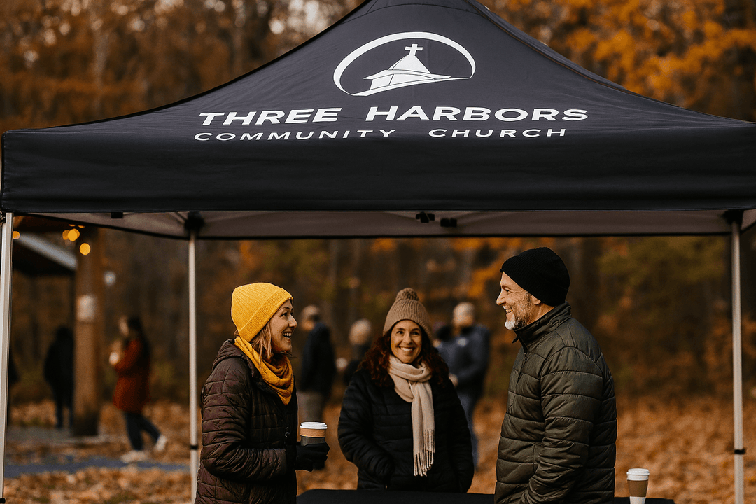 Three people standing under a 'Three Harbors Community Church' tent in an outdoor setting.