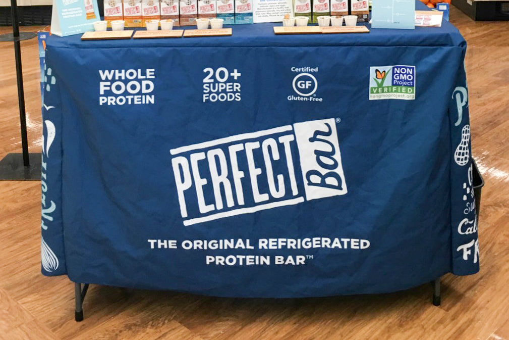 Promotional booth with a blue Perfect Bar convertible table cover, product samples on top