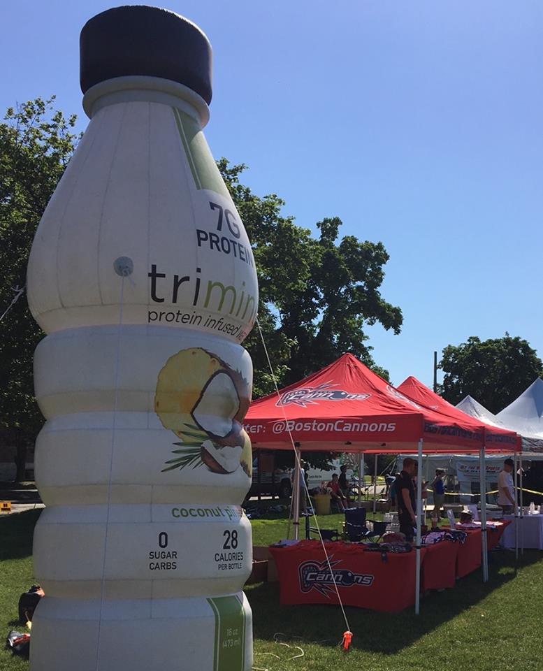 Giant inflatable protein-infused drink advertisement at a sunny farmers' market event