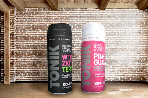 Two large inflatable promotional cans for TONIK drinks, black and pink, inside a room with brick walls