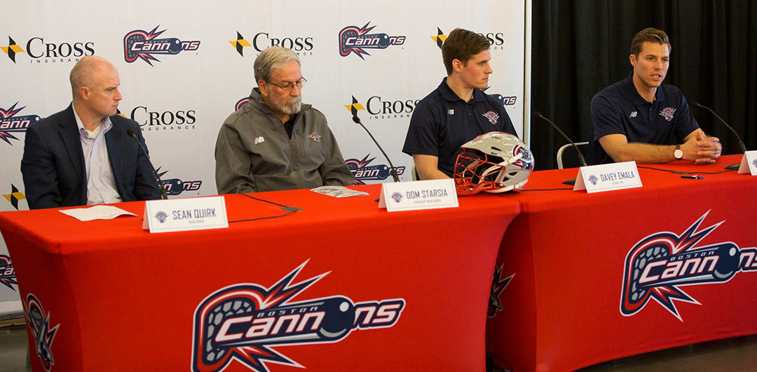 Cannons team members seated at a branded red table for a press conference, with name tags in front of each person