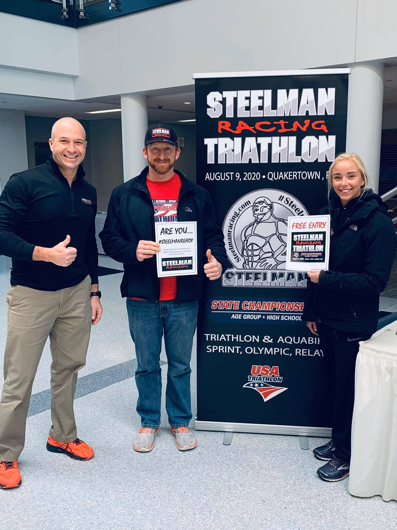 steelman racing triathlon customized roll up banner with two employees and an attendee standing next to it