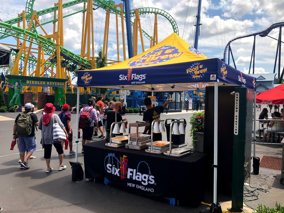 concession tent at Six Flags with 'Food & Brew' banner and thrill rides in background