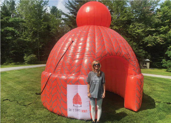 Woman posing with a large inflatable red beanie hat at an outdoor event