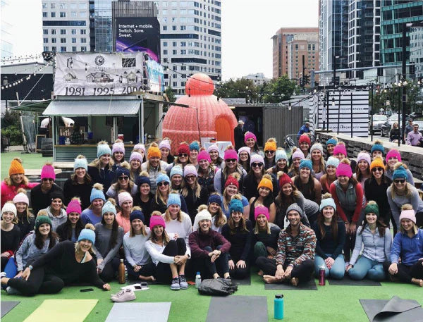 Group photo of people wearing colorful beanies in front of a large inflatable beanie hat at an outdoor event