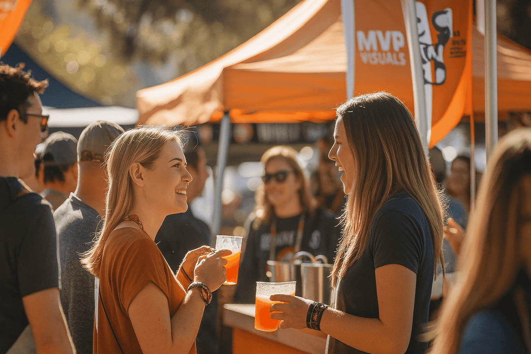 Attendees chatting at an outdoor event under an orange canopy featuring the MVP Visuals logo