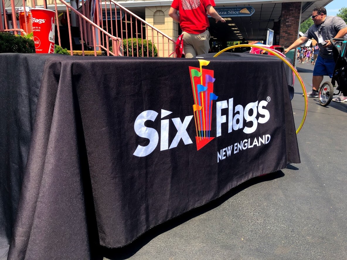 Table covered with a black cloth displaying the Six Flags New England logo at an outdoor amusement park event
