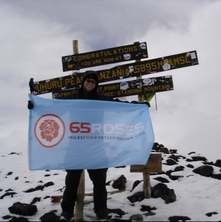 Person holding 65 Roses vinyl mesh banner at snowy Uhuru Peak summit on Mount Kilimanjaro