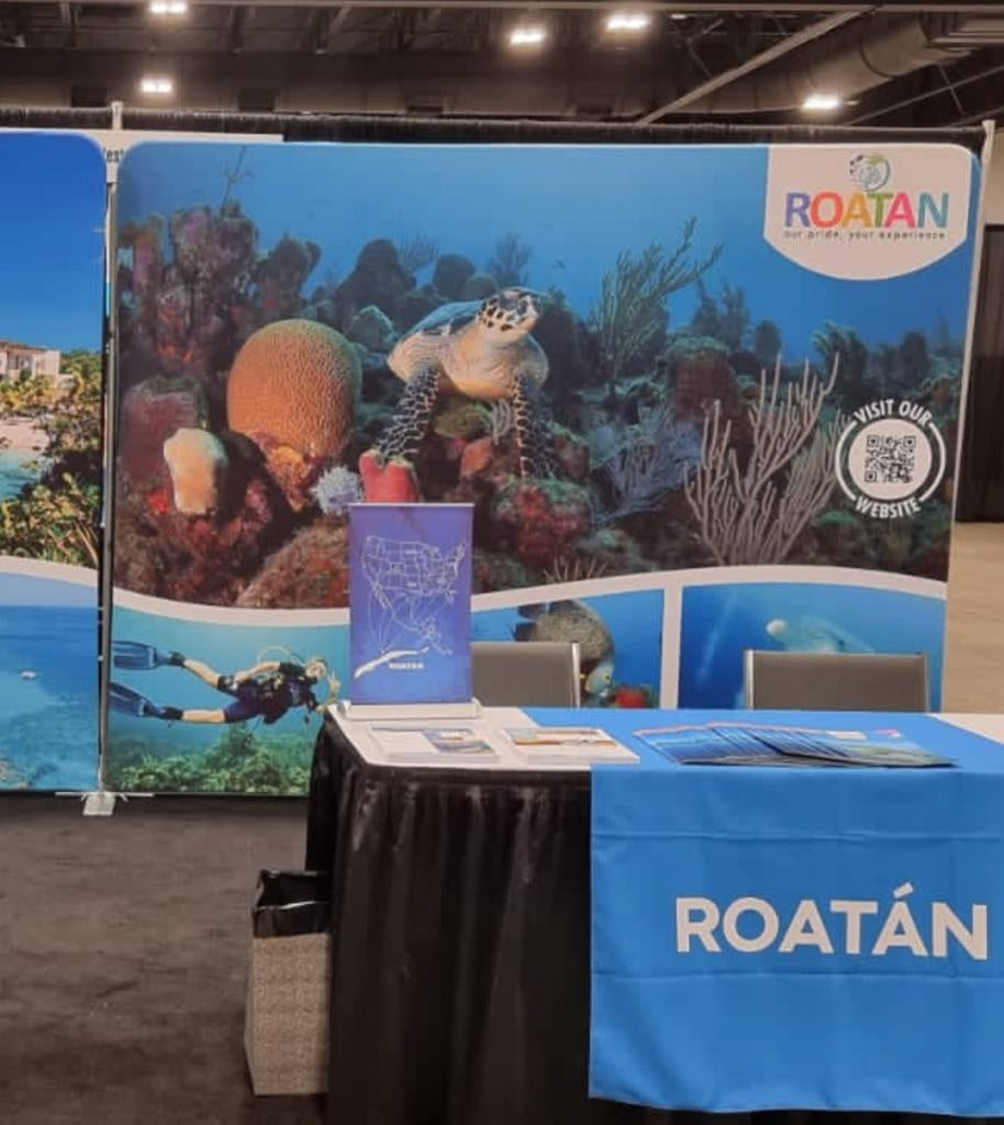 A 10 x 10 tension pop up banner featuring vibrant underwater imagery for Roatan tourism, displayed at a trade show