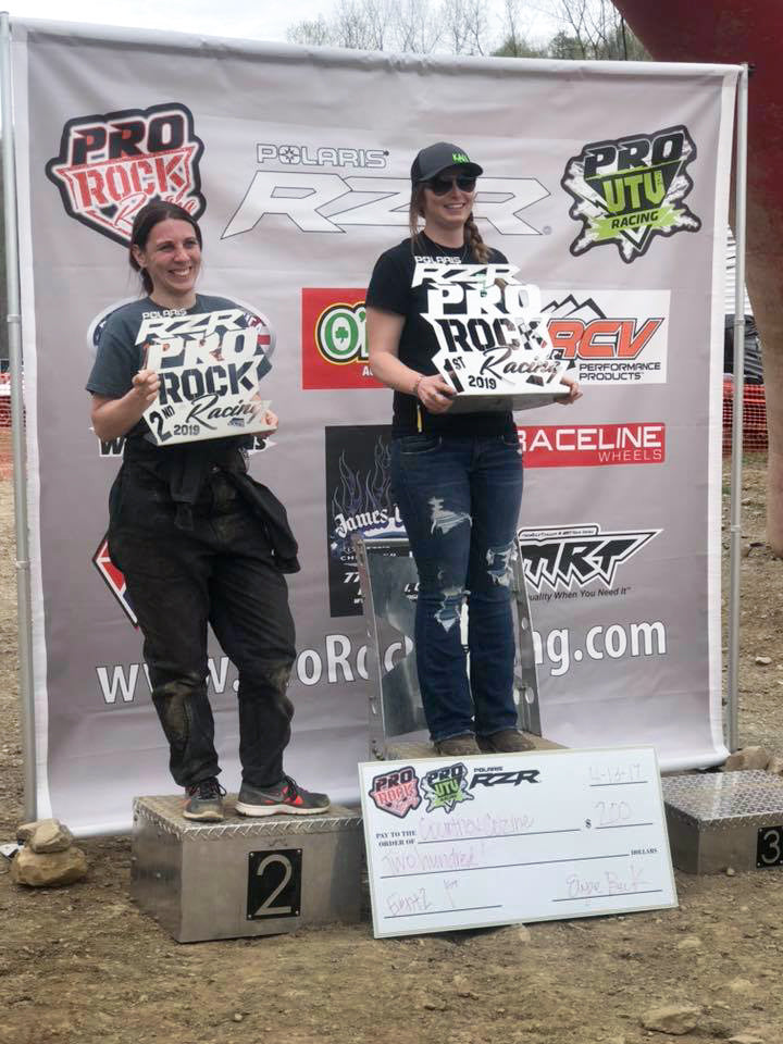 First and second place winners at PRO ROCK Racing event, posing in front of a sponsored banner with various racing logos