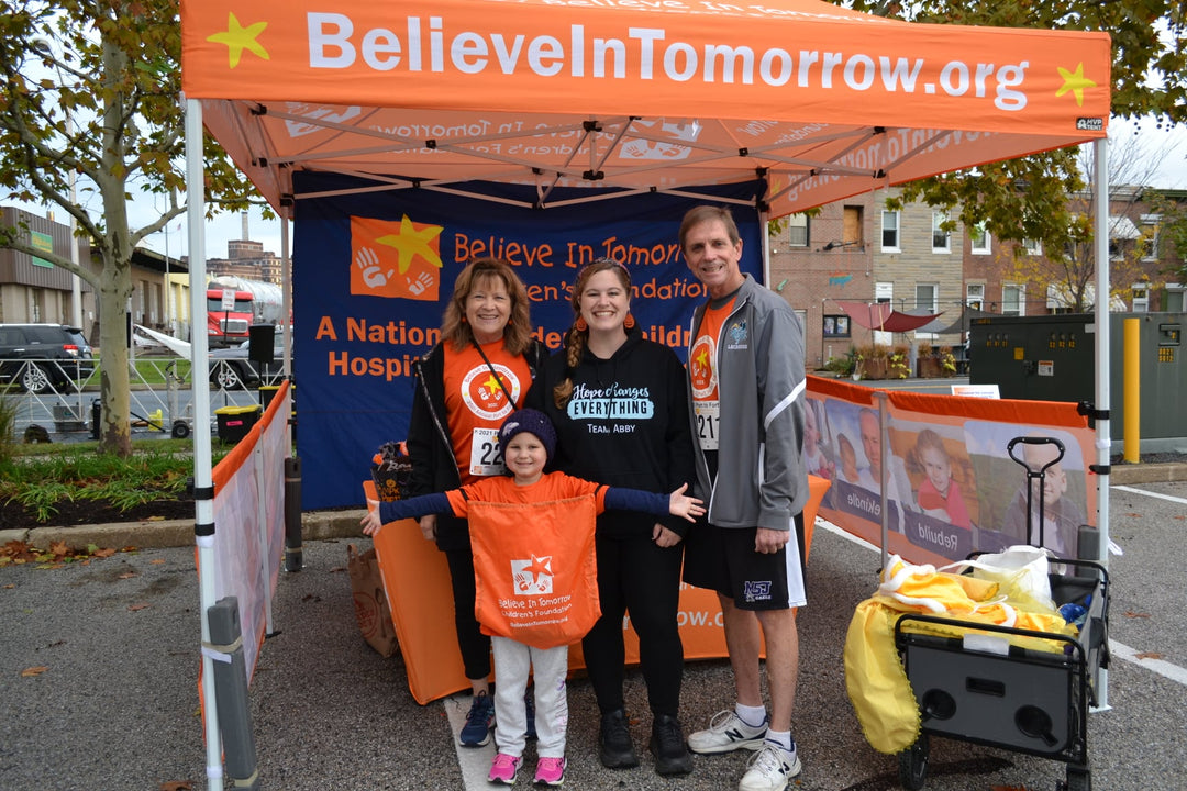 A family smiling under a Believe In Tomorrow custom canopy at a nonprofit charity event.