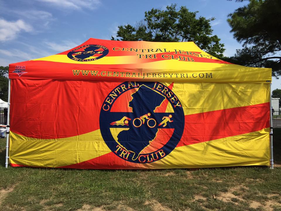 A vivid Central Jersey Tri Club 10 x 20 triathlon tent with logo, under a clear sky, symbolizing community and sportsmanship