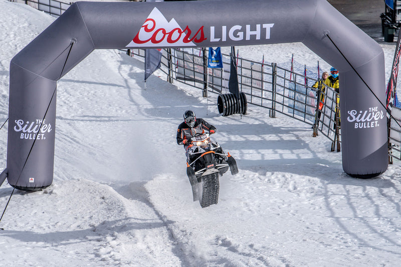 Snowmobile racer passing through a Coors Light branded inflatable archway at a winter sports event