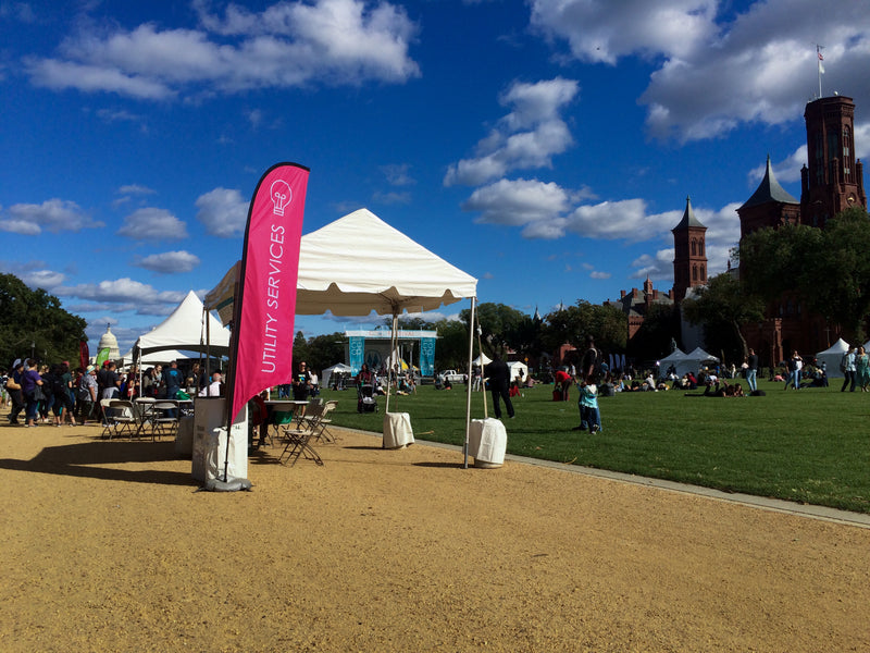 Outdoor scene with a pink UTILITY SERVICES feather flag, and white tent in university campus under a blue sky