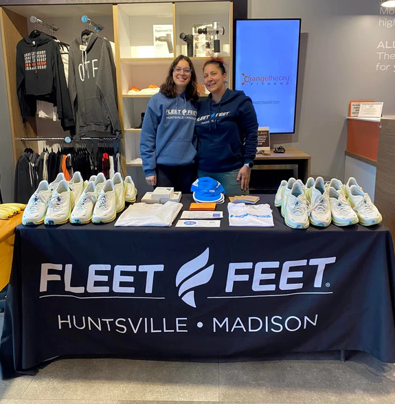 Logo tablecloth for trade shows with Fleet Feet Huntsville Madison branding, presented by smiling staff