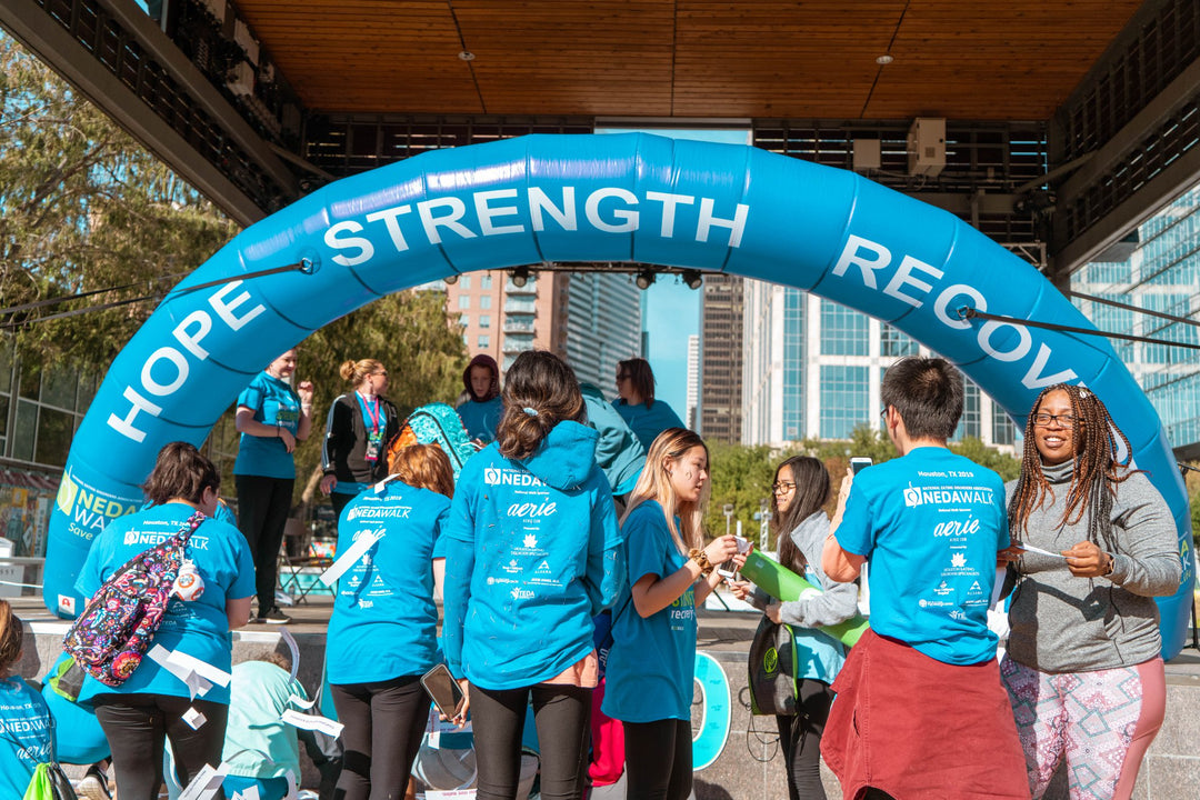 Participants at NEDA's Walk to Save a Life event passing under a round inflatable arch with HOPE STRENGTH RECOVERY printed on it.