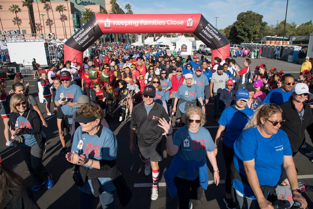 Crowds of participants at Ronald McDonald House Orange County walk event passing under a red inflatable arch with Keeping Families Close slogan.