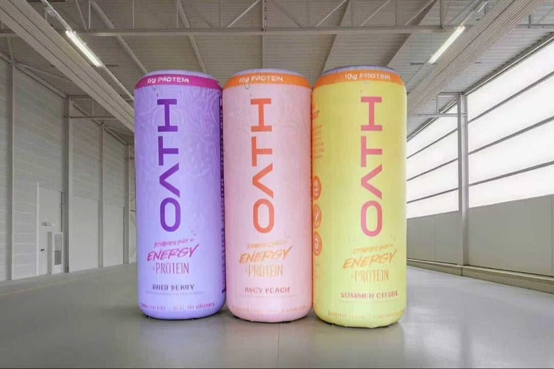 Three OATH protein tubs in purple, pink, and yellow on a concrete floor with large windows in the background.