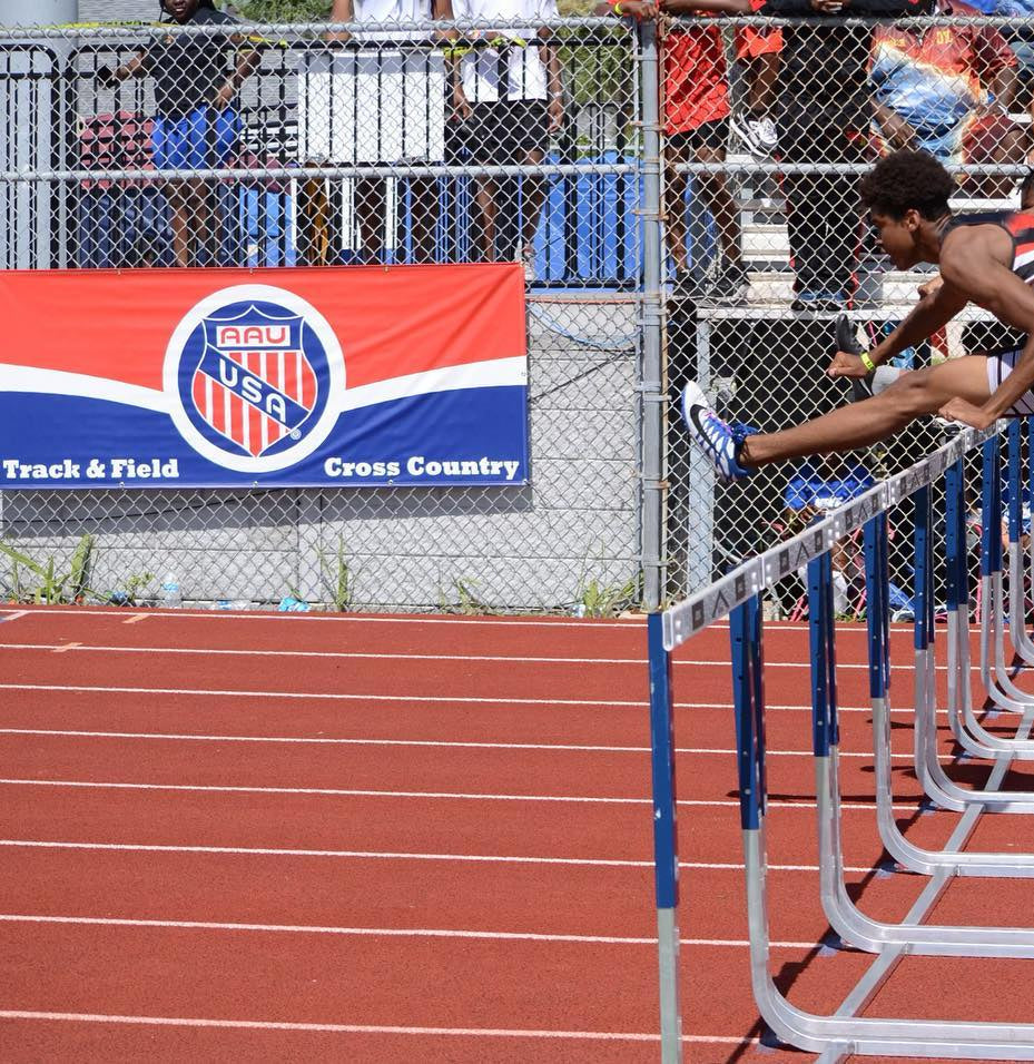 Two male athletes mid-air clearing hurdles during AAU Track and Field Championship race