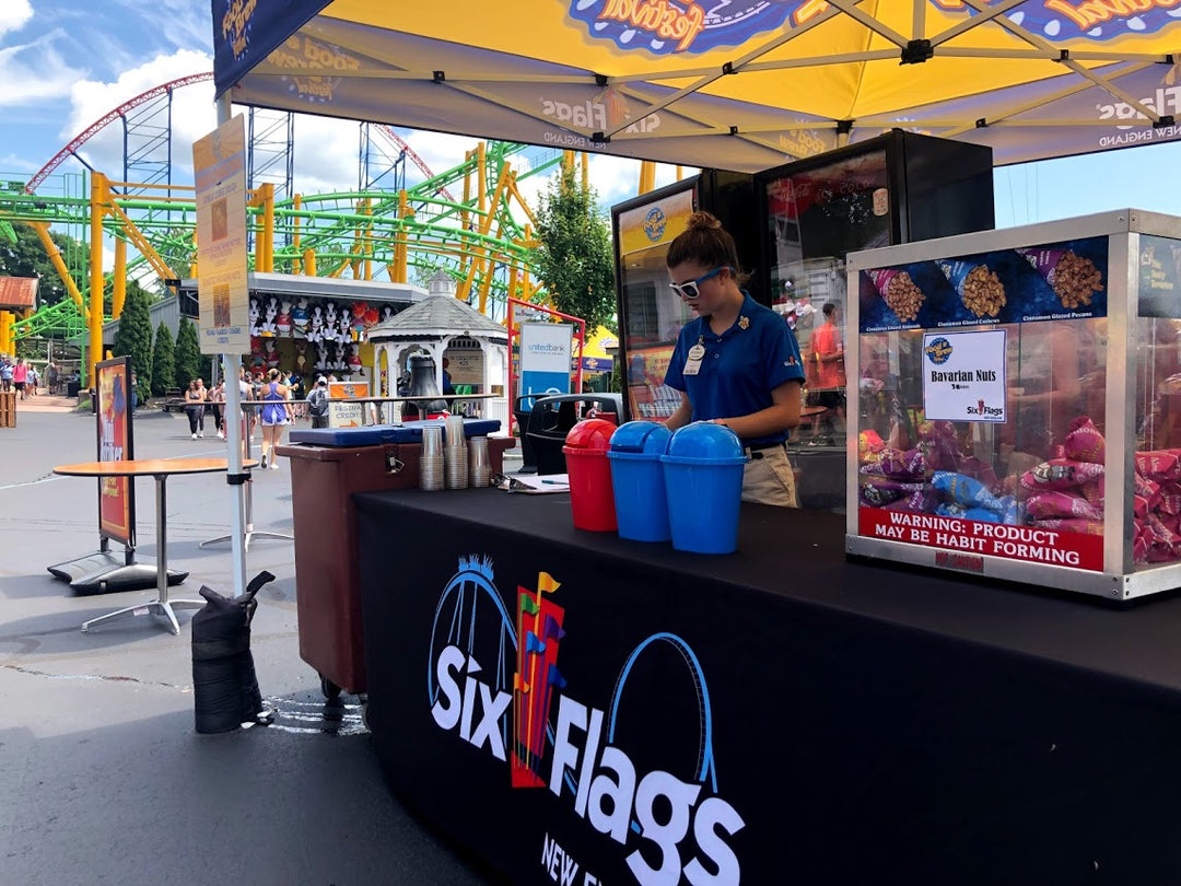 Six Flags themed concession stand tent with staff and rollercoaster backdrop