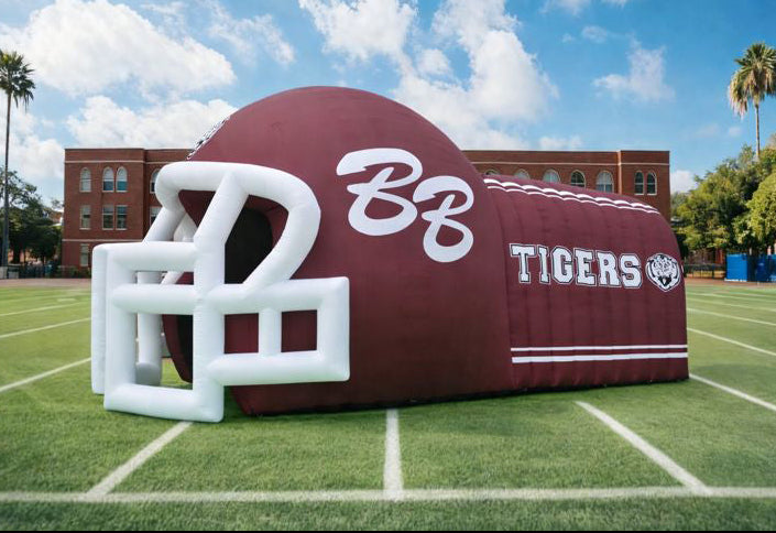 Inflatable football helmet and tunnel with 'BB Tigers' branding on a sports field.