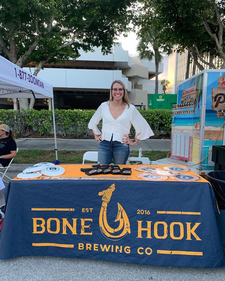 Woman standing behind a table with Bone Hook Brewing Co branding at an outdoor event.