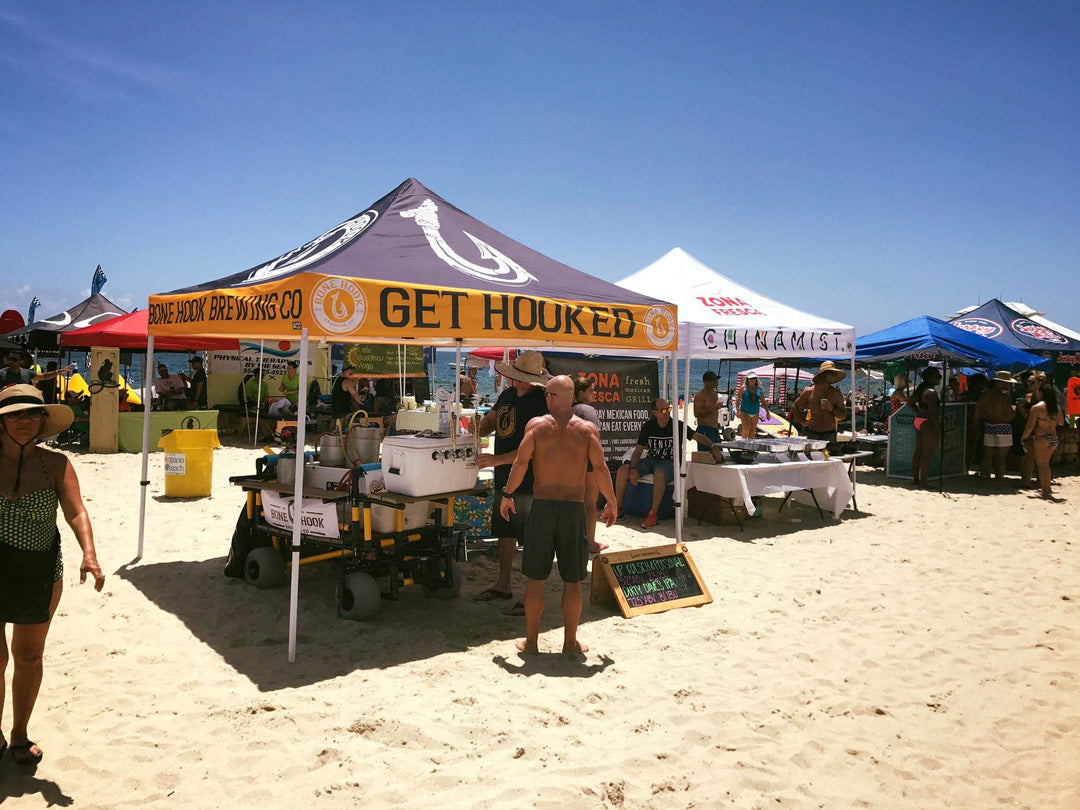 Bone Hook Brewing Co custom canopy tent at sunny beach festival with branded “Get Hooked” design and crowd activity