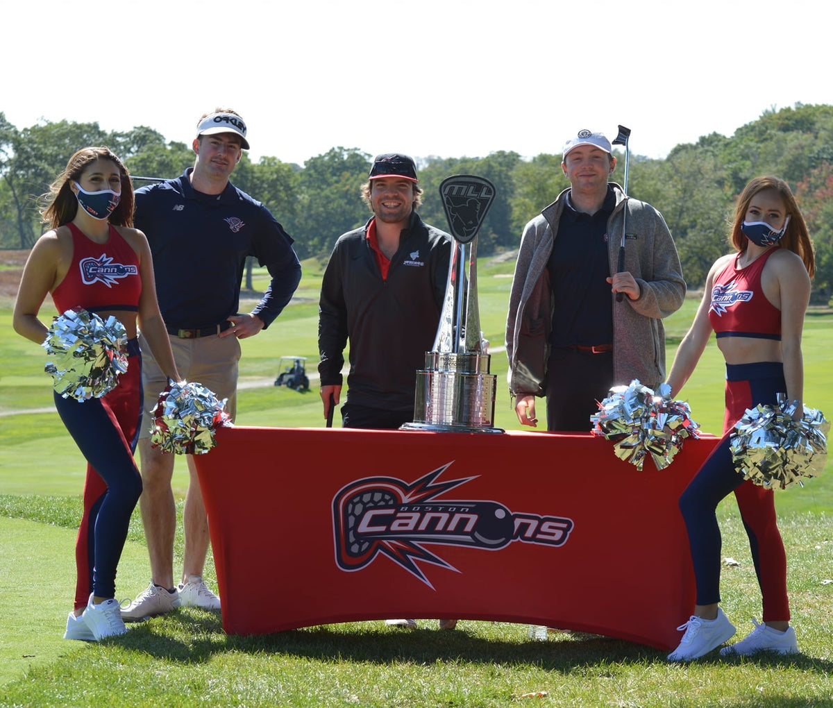 Group of people with a trophy on a golf course, featuring the 'Cannons' logo.