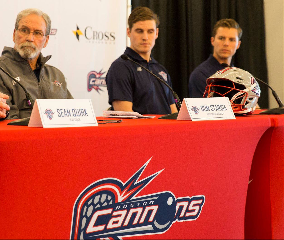 Press conference with four men at a table with Boston Cannons branding