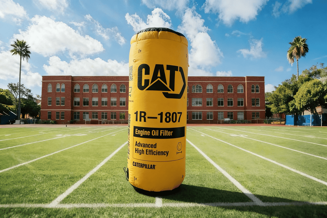Large yellow Caterpillar oil filter custom inflatable on a sports field with a building in the background
