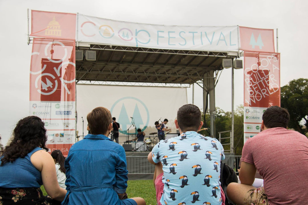 Audience watching live music performance at Co-op Festival under vinyl mesh stage banners
