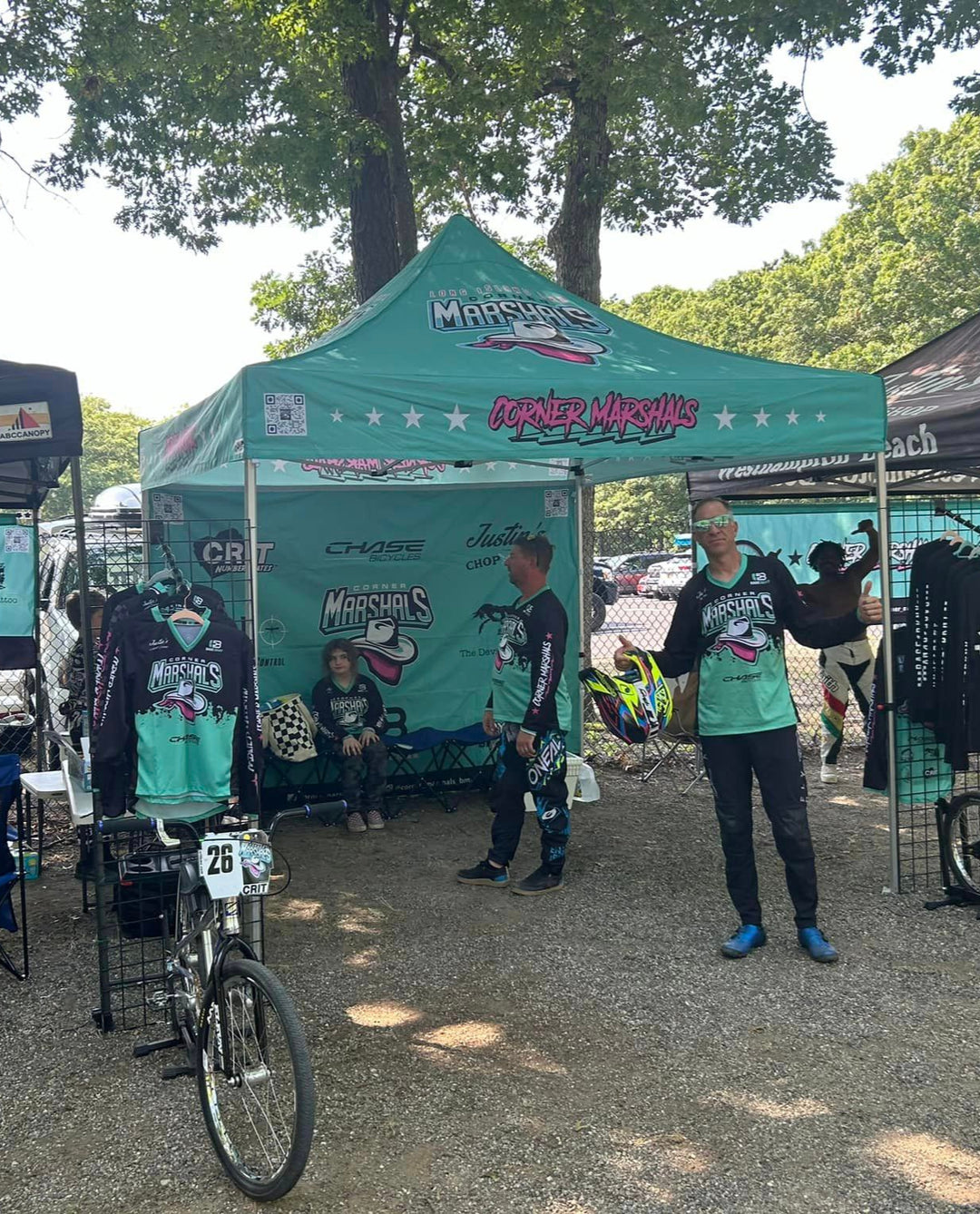 Corner Marshals BMX team event setup featuring custom MVP Visuals canopy tent with printed back wall, jerseys, and bikes at outdoor race venue