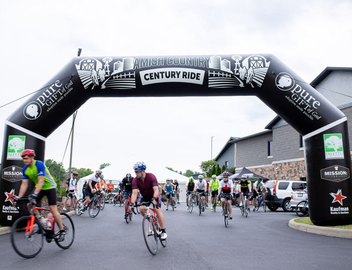 Cyclists starting Amish Country Century Ride under custom black inflatable arch with sponsor logos