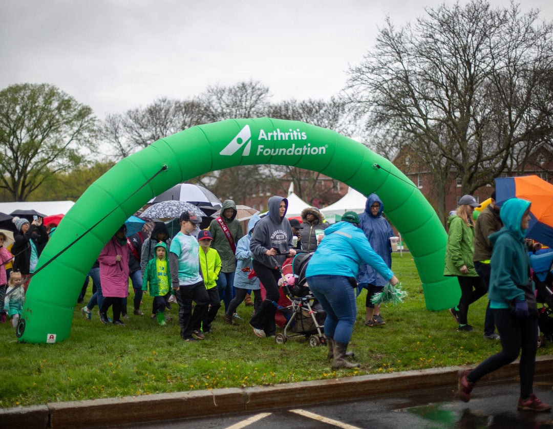 Participants walking under custom green inflatable arch at Arthritis Foundation event on a rainy day