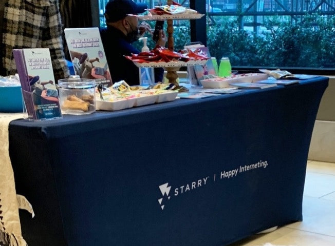 Custom spandex table cover for Starry internet booth with snacks and marketing materials beside a pet pig.