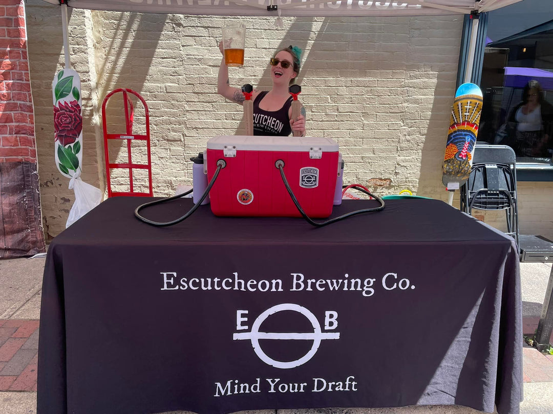 Custom table cover for Escutcheon Brewing Co. outdoor event booth with draft beer station and server holding pitcher