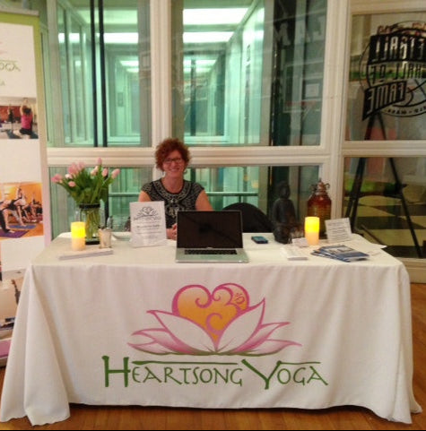 Custom table cover with Heartsong Yoga logo at indoor wellness event booth with flowers and candles