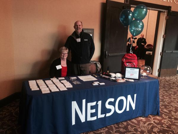 Custom table cover with Nelson branding at indoor event booth featuring giveaway items and informational materials